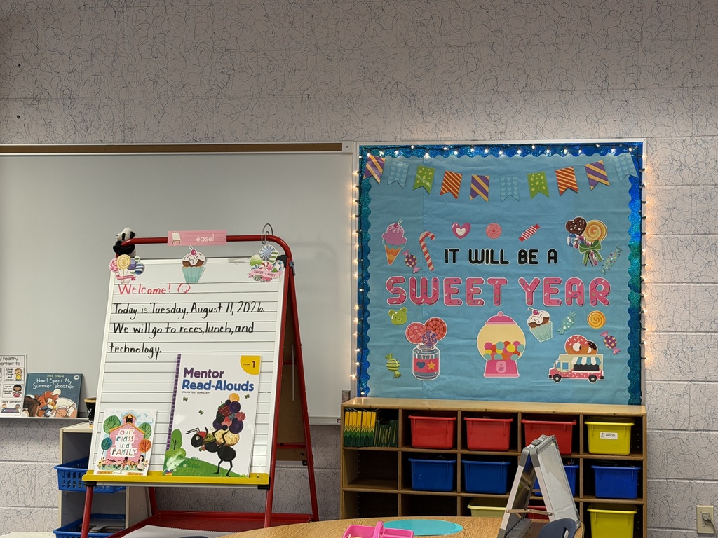 A classroom with a whiteboard, a bulletin board with decorations, and a table with a computer.