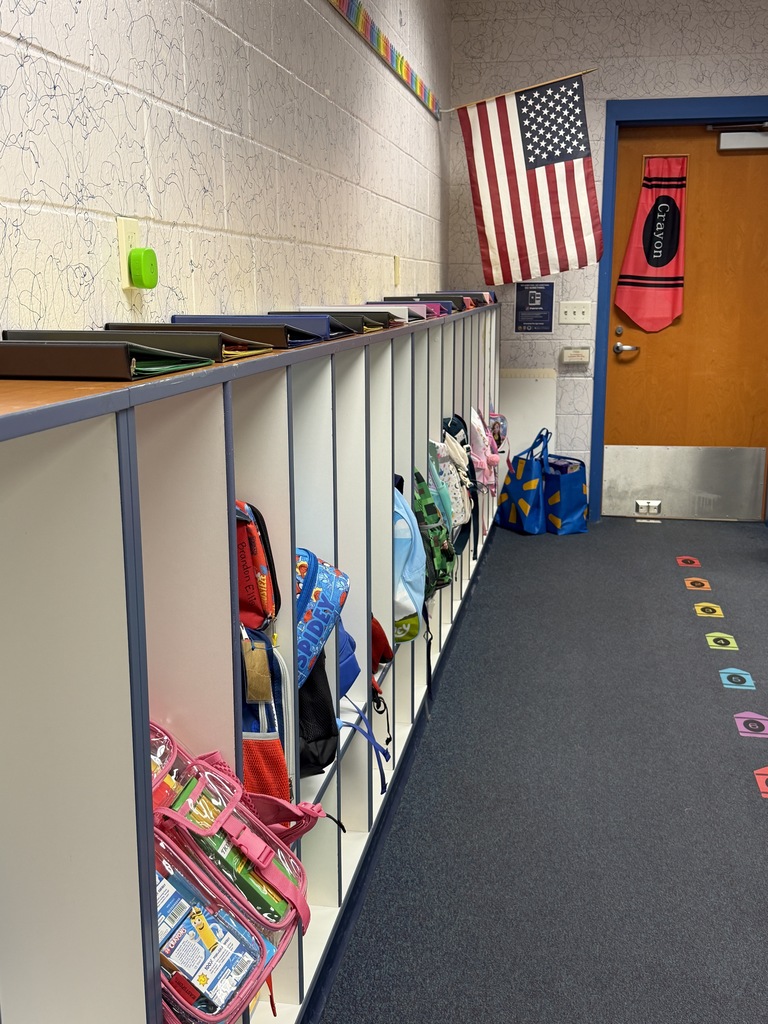 A hallway with lockers on the left and a US flag hanging on a wall. Colorful shapes on the floor.