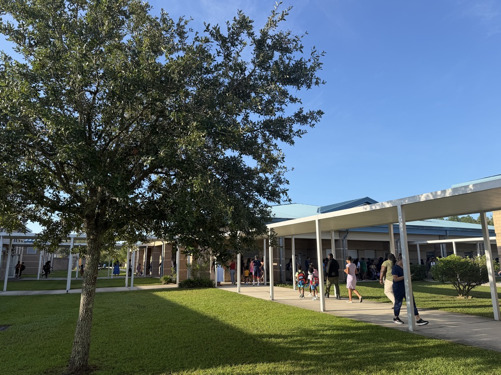 Green lawn with people walking under awnings. Trees, a building, and a clear blue sky.