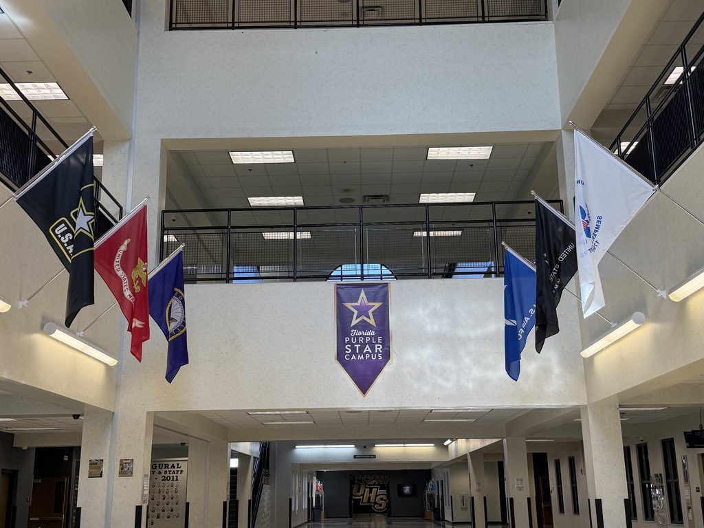 Interior of a building with banners and flags hanging from the ceiling. Flags include purple with text, white with text, and blue and white.