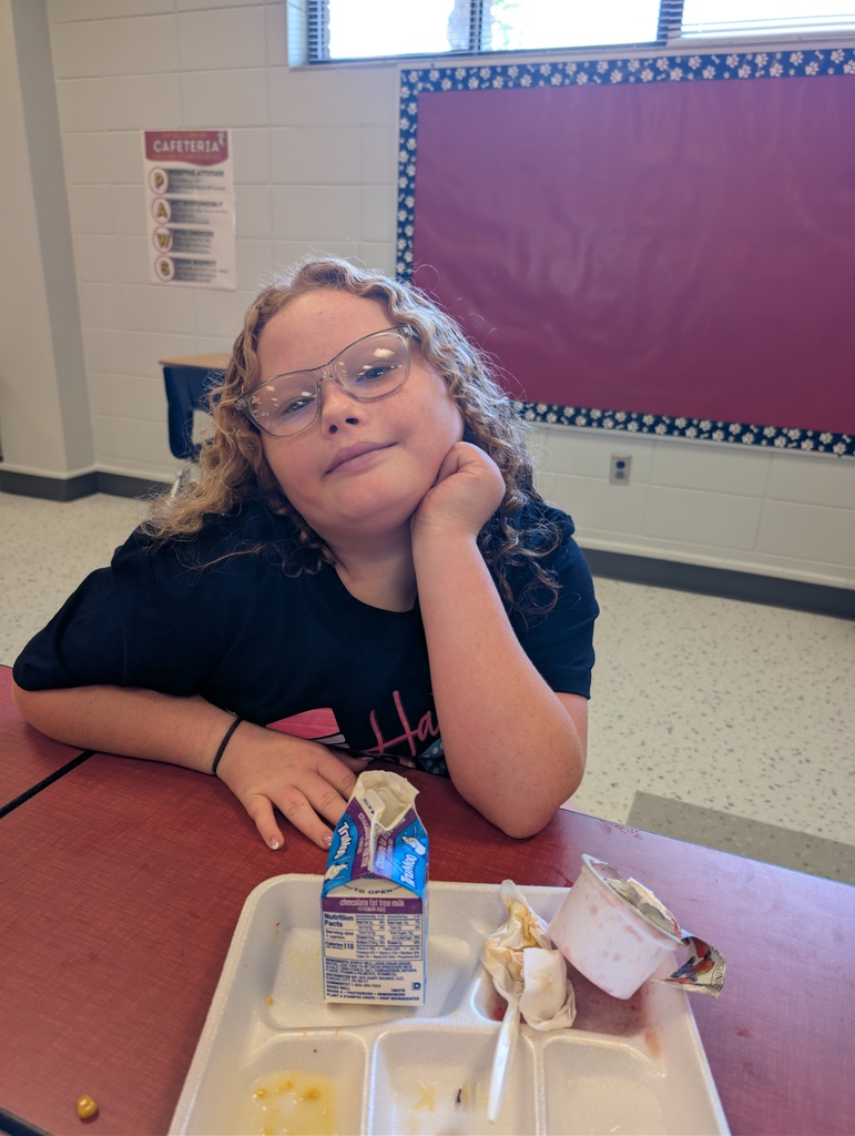 A person with glasses sits at a table, wearing a black shirt, and looks at the camera.