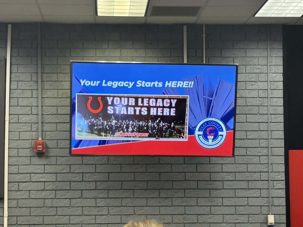 Large screen on a brick wall showing a message with a band image. Fire extinguisher on left.