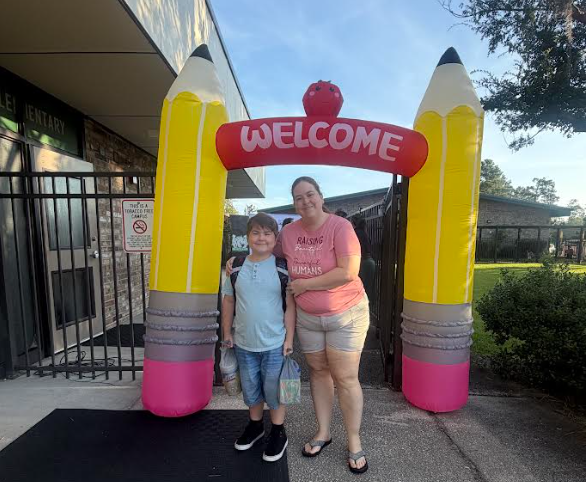 A person and a child stand under a colorful arch labeled "WELCOME" outside a building.