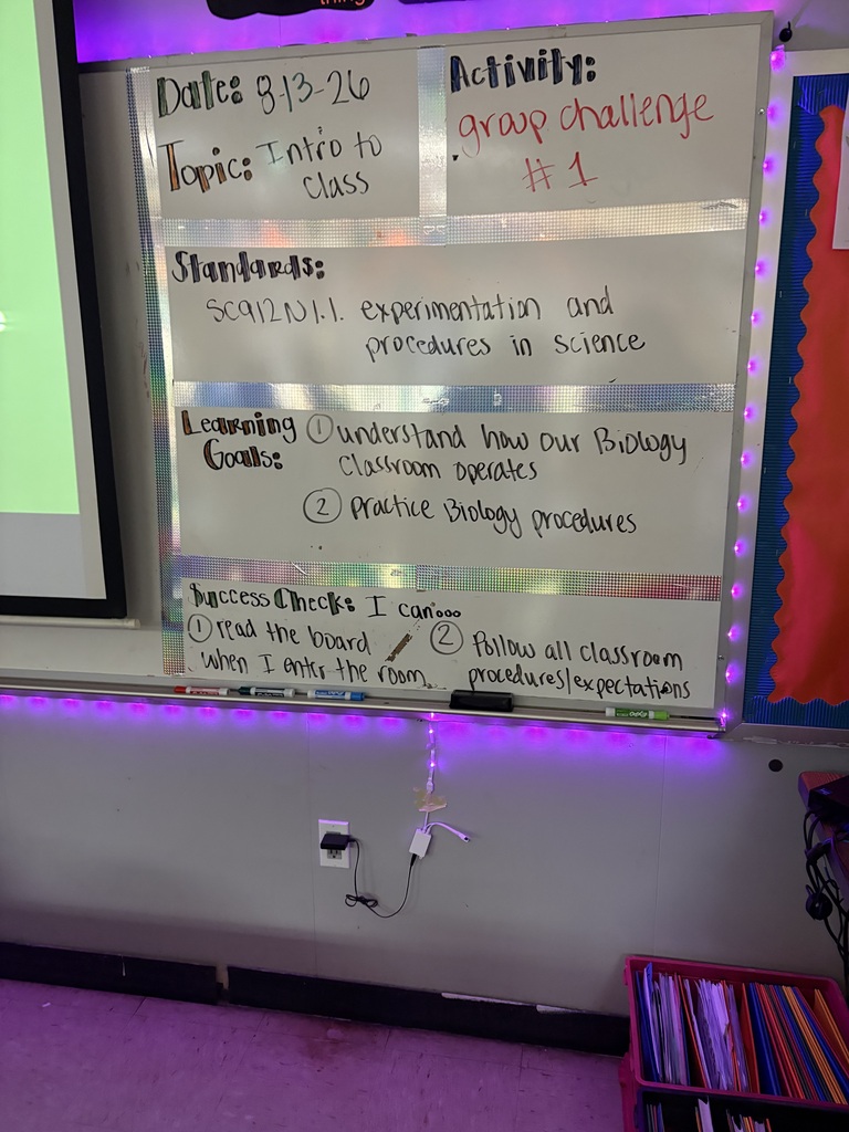 A white board with white chalk writing is on a wall. The board has information about dates, topics, and activities.