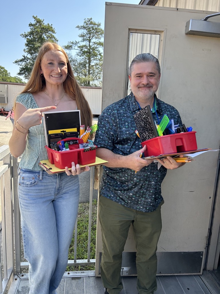 A man and woman stand on a porch holding trays with various school supplies. They are smiling.