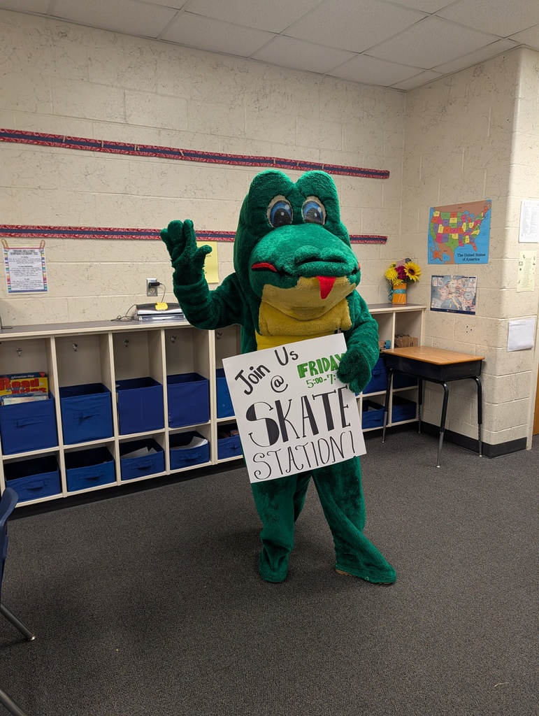 A mascot dressed as a frog holds a sign that says "Join Us @ FRIDAY SKATE STATION" inside a classroom.