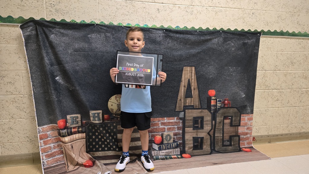 A child holds a framed certificate in front of a backdrop featuring bricks and the word ABC.