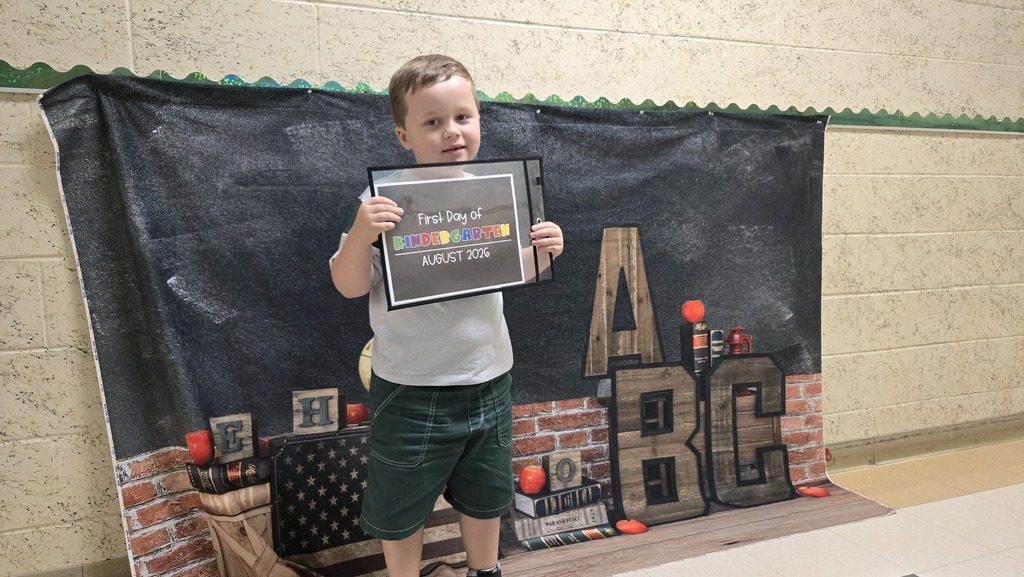 A young child holding an award plaque in front of a black banner with colorful letters.