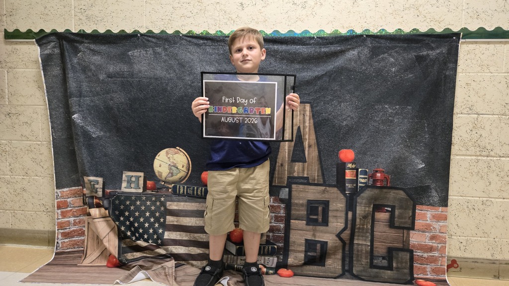 A child holds a framed certificate in front of a backdrop with a black background and ABC letters.