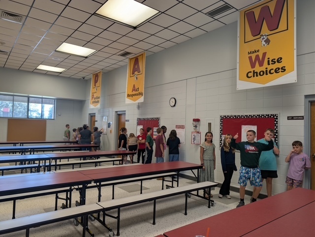 A room with tables and benches. Banners reading "Wise Choices" and "A" are hanging on the wall.