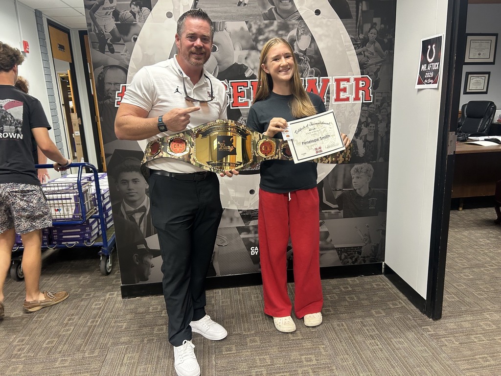 A man and a woman stand in a room, posing with a belt and certificate. They are in front of a large mural.