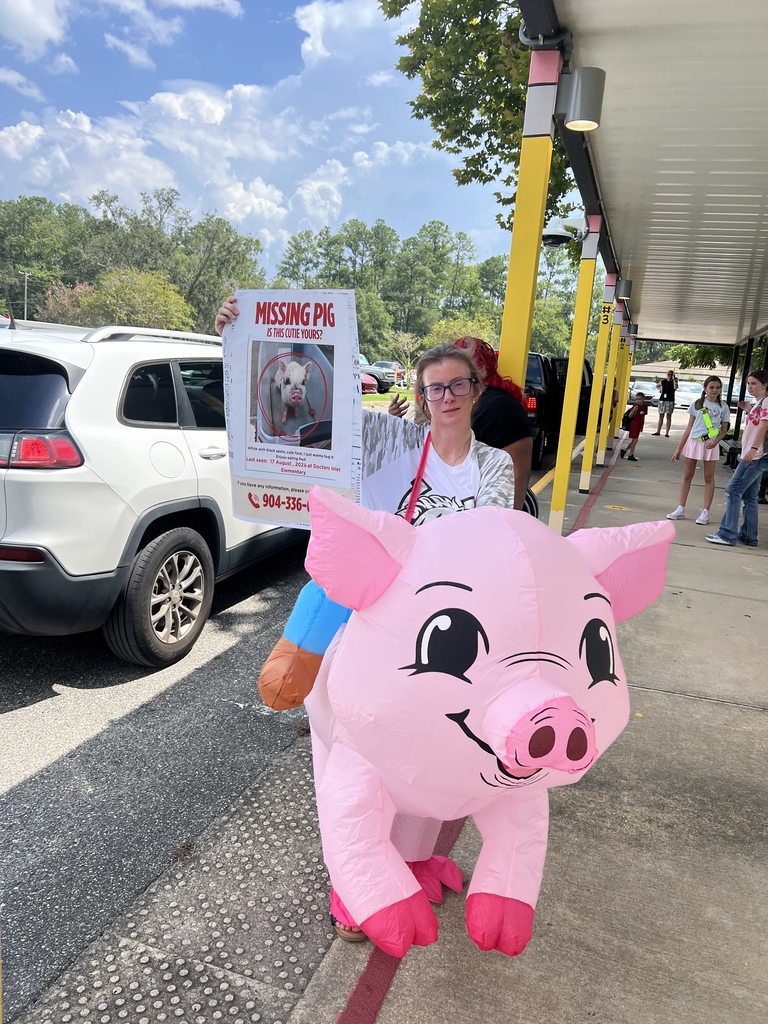 Person in pig costume holding a poster with a missing dog picture. A white SUV and buildings in the background.