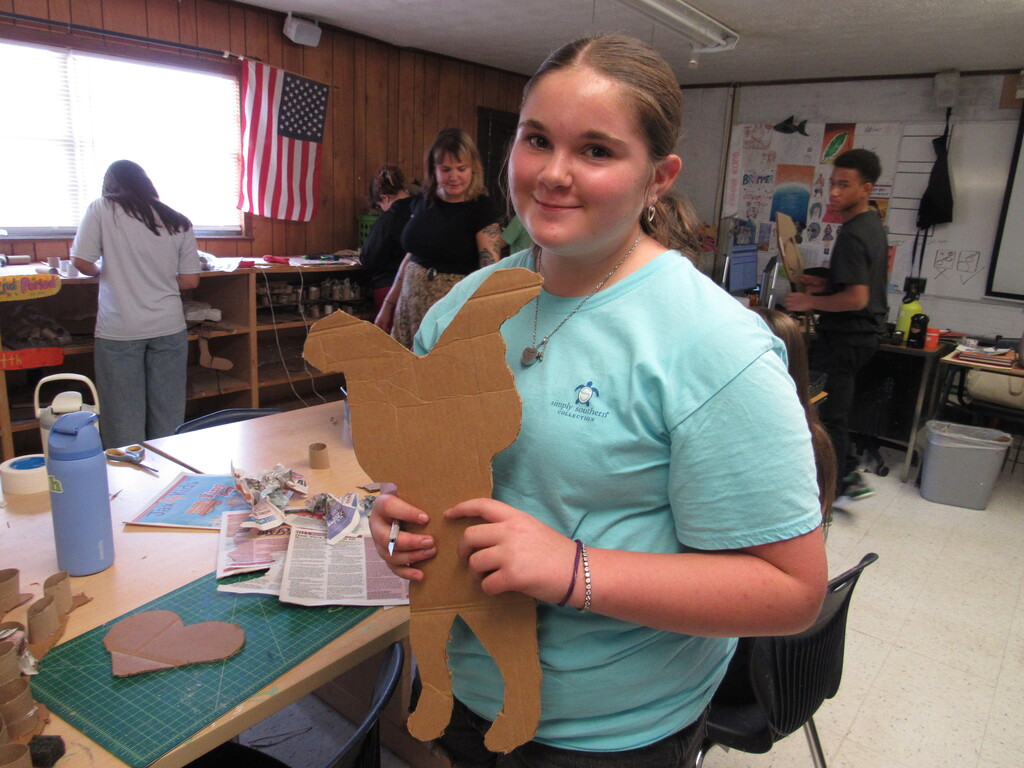 Woman wearing a light blue t-shirt stands in front of a table, holding a cutout of a camel.