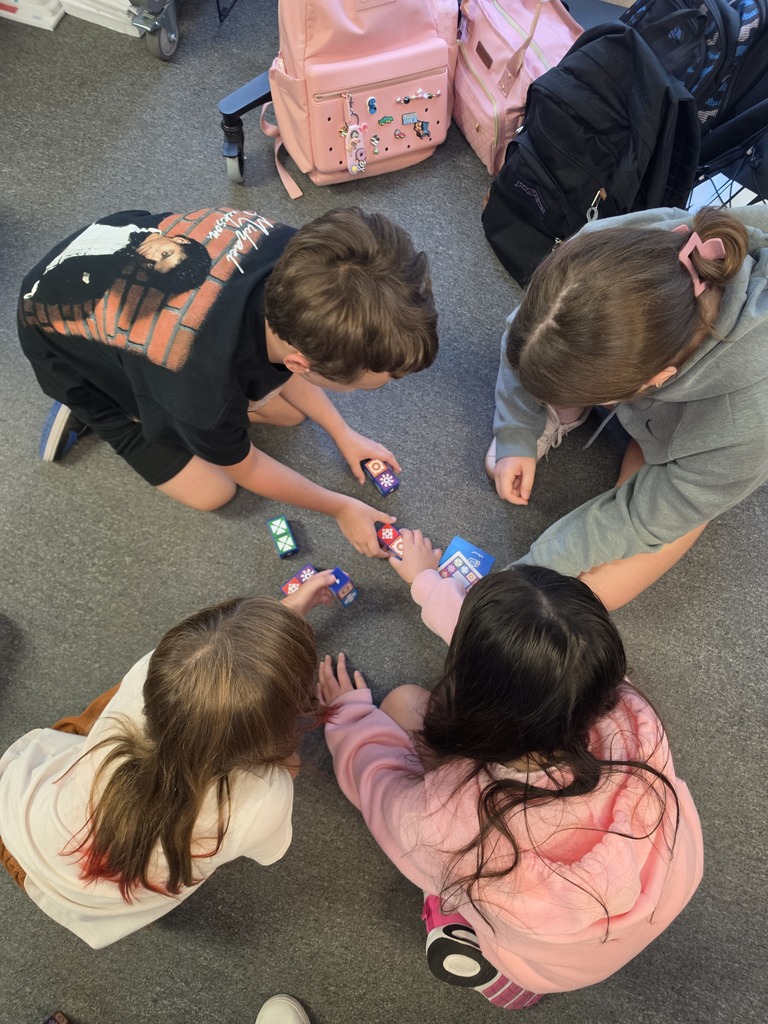 Four children play with small toys on a carpeted floor, surrounded by school bags.
