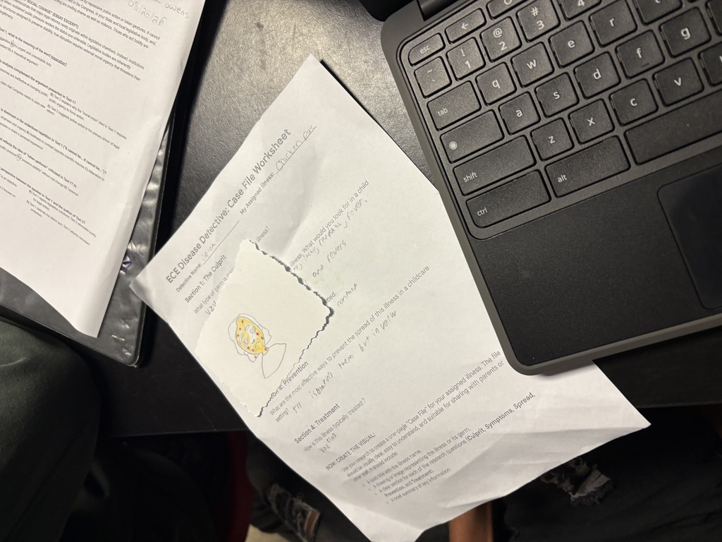 A piece of paper with printed text lies next to a laptop on a table. A partially visible document and plastic bag are also present.