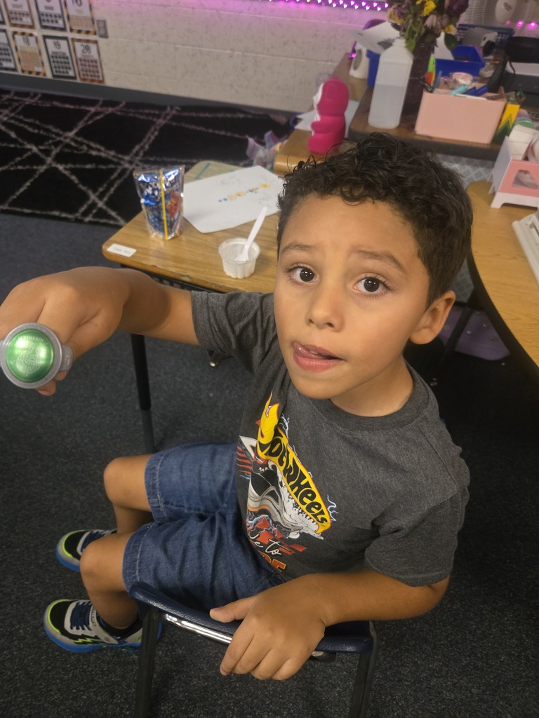 A young boy is sitting in a chair holding a green flashlight. He is wearing a gray shirt.