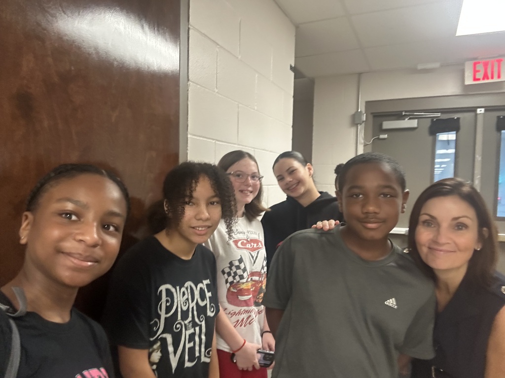 A group of students in matching T-shirts stands in front of a door with an exit sign.