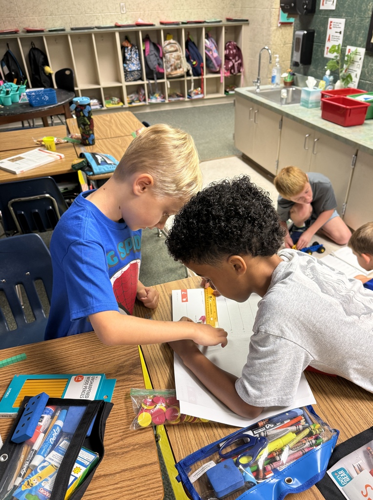 Three boys at desks in a classroom. One boy looks at another boy's paper.