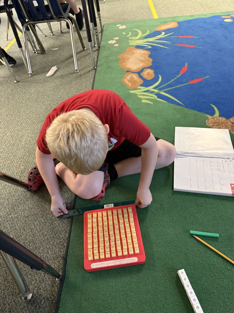 A boy on a rug with a pencil, a book, and a red tile abacus.