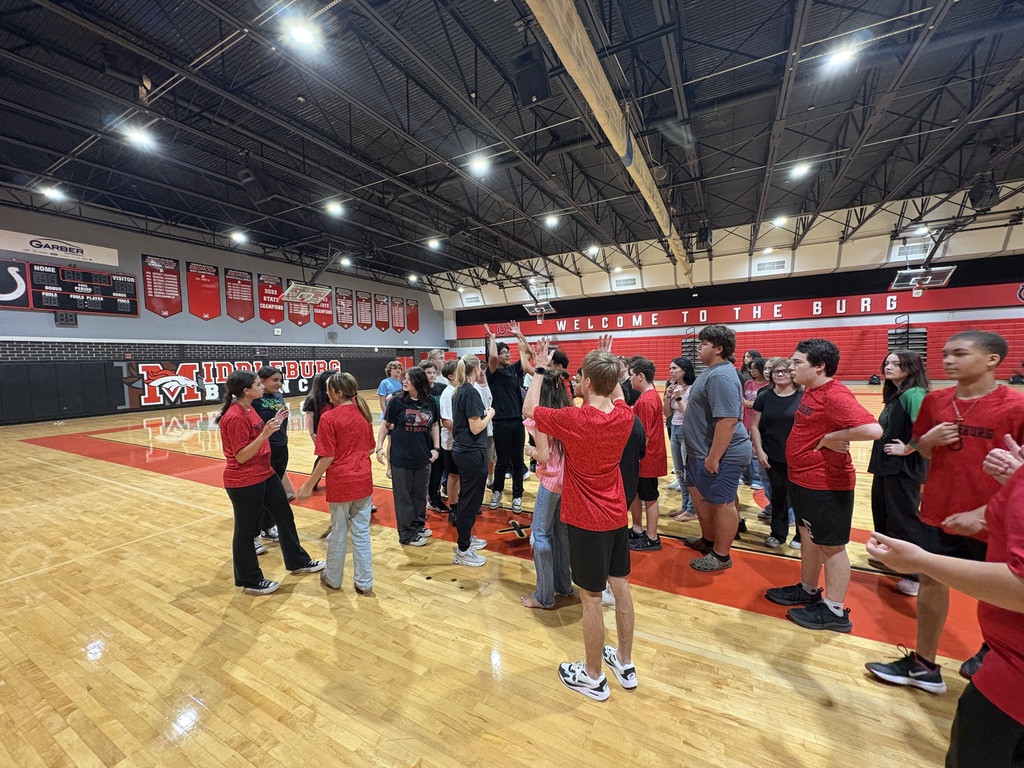 A group of people in red shirts and sneakers gathered on a basketball court, possibly engaging in a team-building activity.