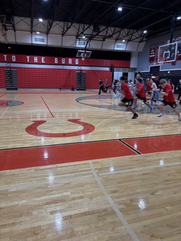 A basketball court with red and white markings. Several people in red shirts are running in a circle.