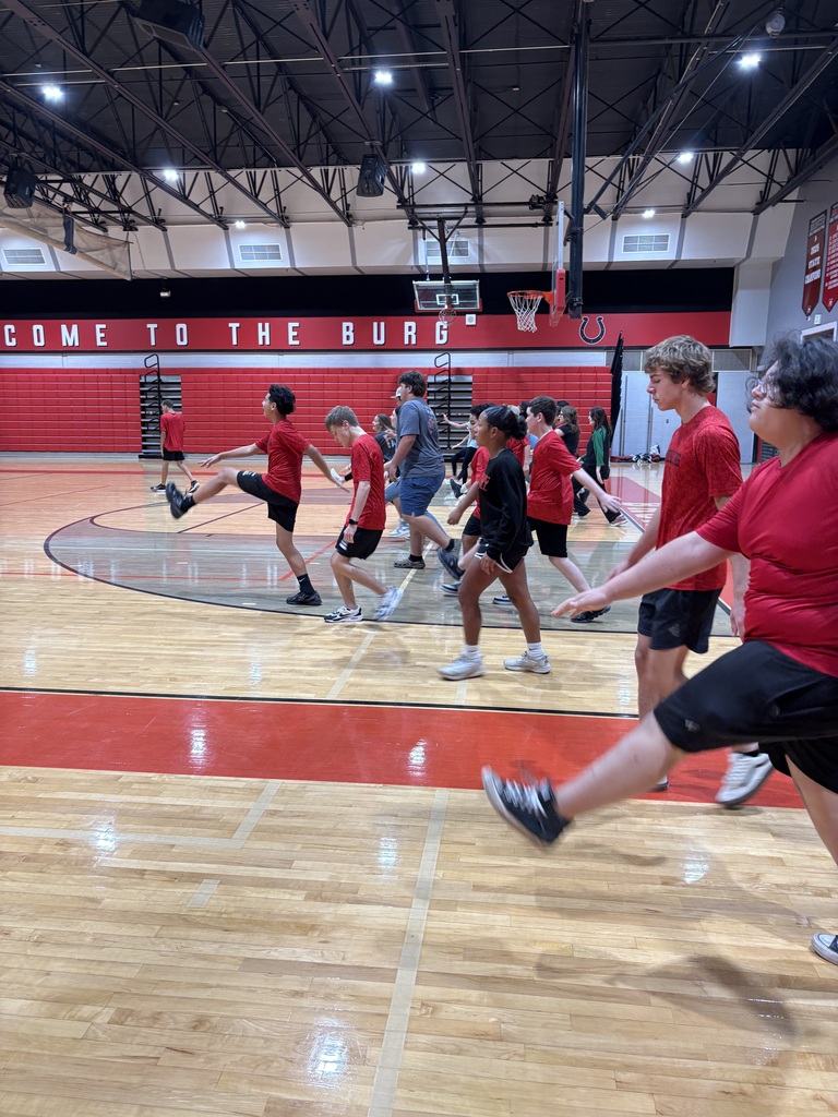 Group of young people in red shirts and black shorts playing a game on an indoor basketball court.