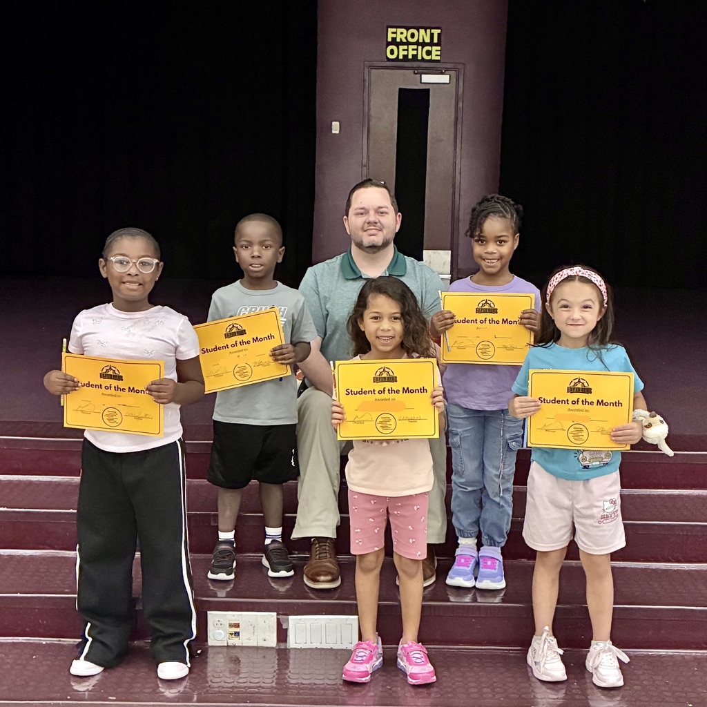 A group of children and a man holding "Student of the Month" certificates stand on stairs.