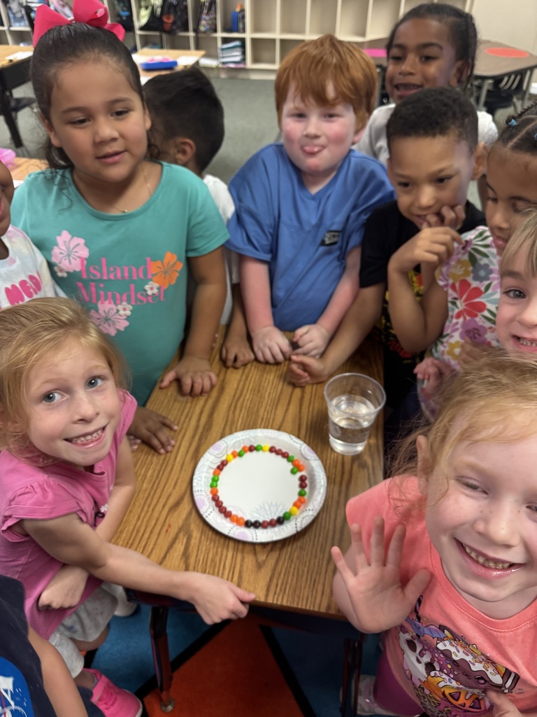 Group of young children around a table, smiling. A plate with colorful beaded artwork sits on the table.