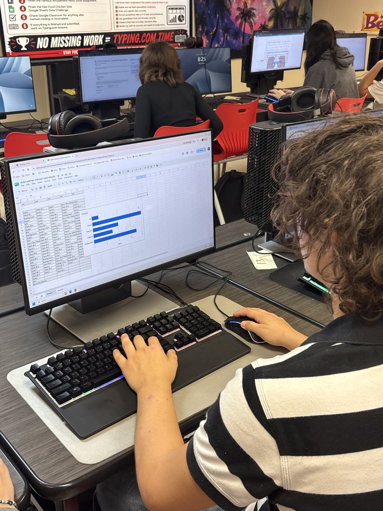 Person wearing a striped shirt using a computer and keyboard at a desk with multiple computers in the background.