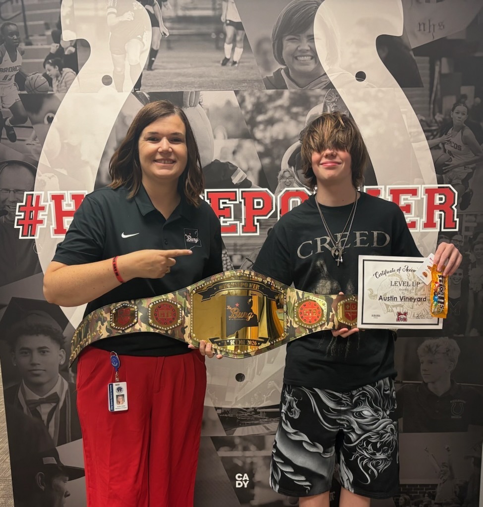 Two young people in sports gear pose with a belt and certificate in front of a sports photo backdrop.