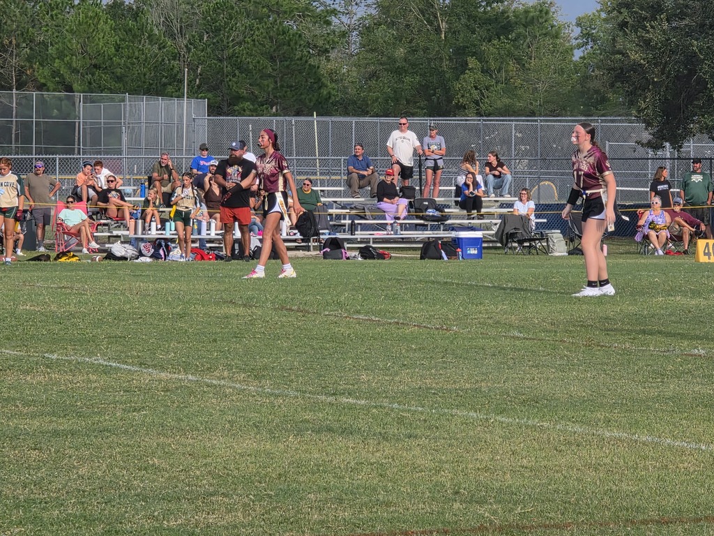 A group of players in jerseys playing a game on a field. A player is bending down. Spectators are watching from bleachers.