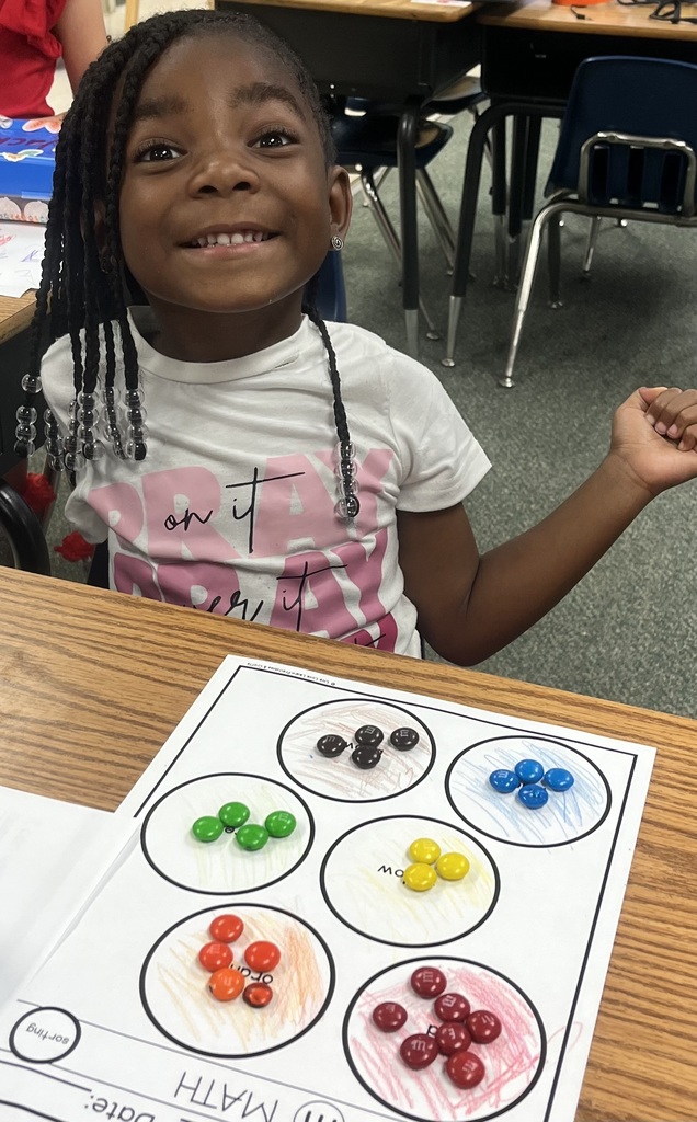 Child sitting at a desk with a math worksheet in front. It shows circles divided into sections with colored candies.