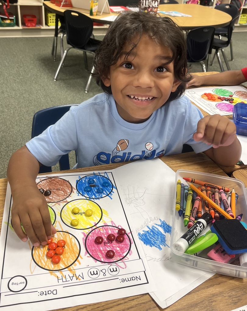 Child seated at a table with a worksheet, crayons, and markers. Worksheet features circles with colorful dots.