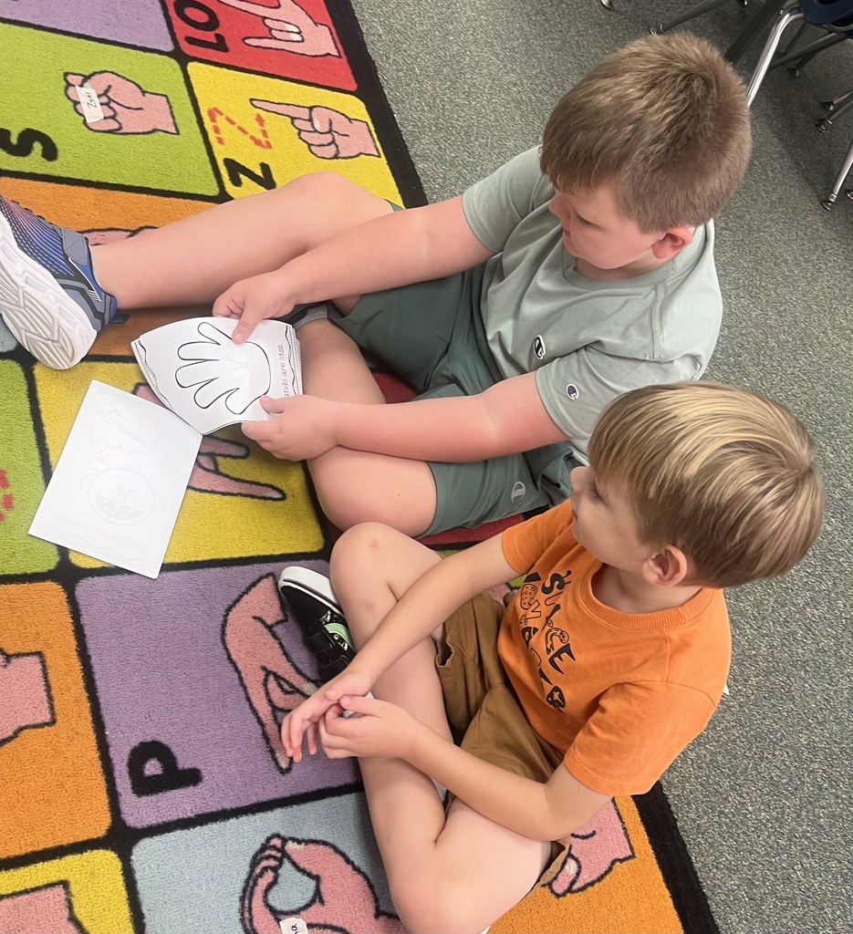 Two boys seated on the floor, engaged in a learning activity with papers and hands-on materials.