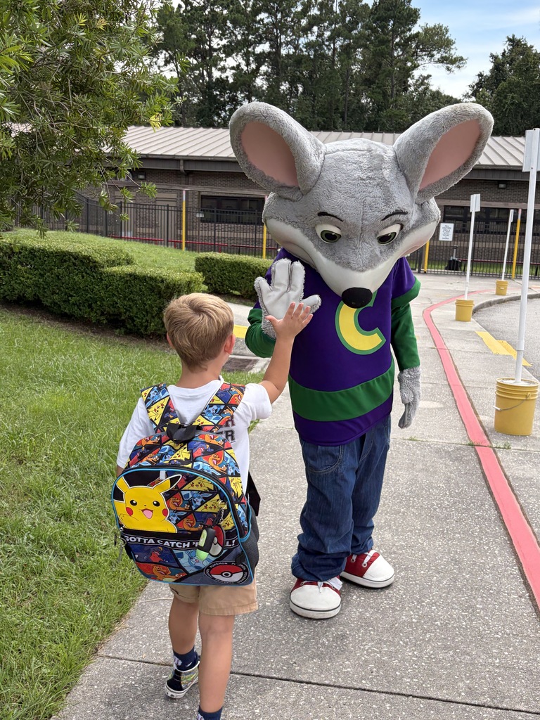 A child wearing a backpack walks on a sidewalk next to a person in a mouse costume.