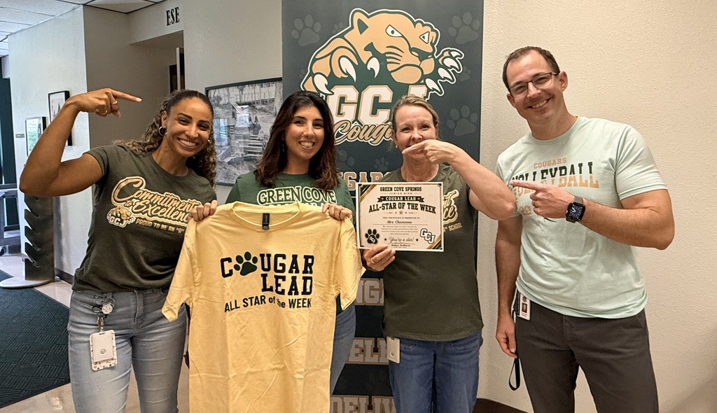 Four people pose with a yellow shirt and a certificate. Two women and two men stand behind a banner with a logo.