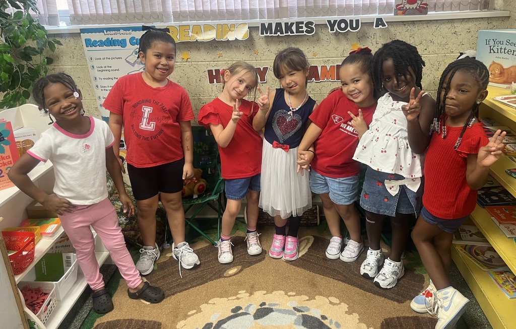 A group of children in red t-shirts pose for a picture. Some wear pink pants and tutus, while others have bracelets.