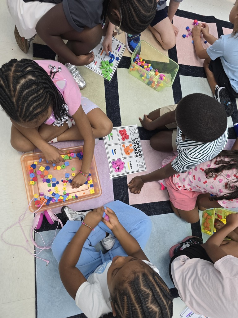 Children sit in a circle on the floor, engaged with a colorful game board and beads.