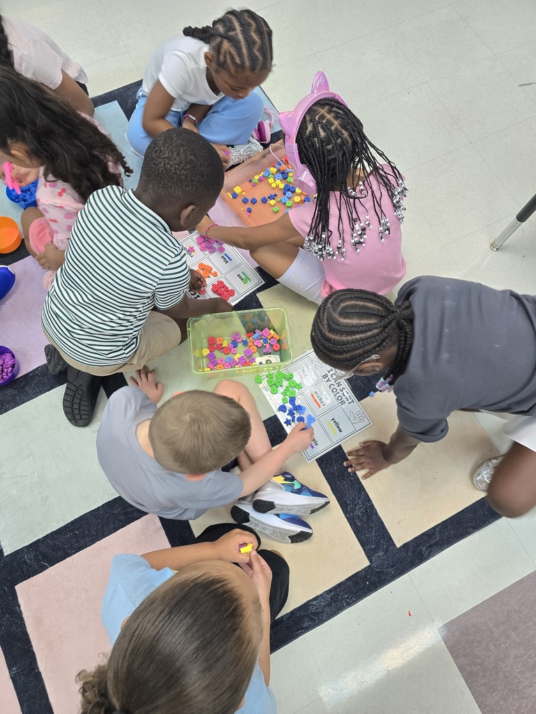 Children and an adult sit in a circle on the floor, working with educational materials and toys.