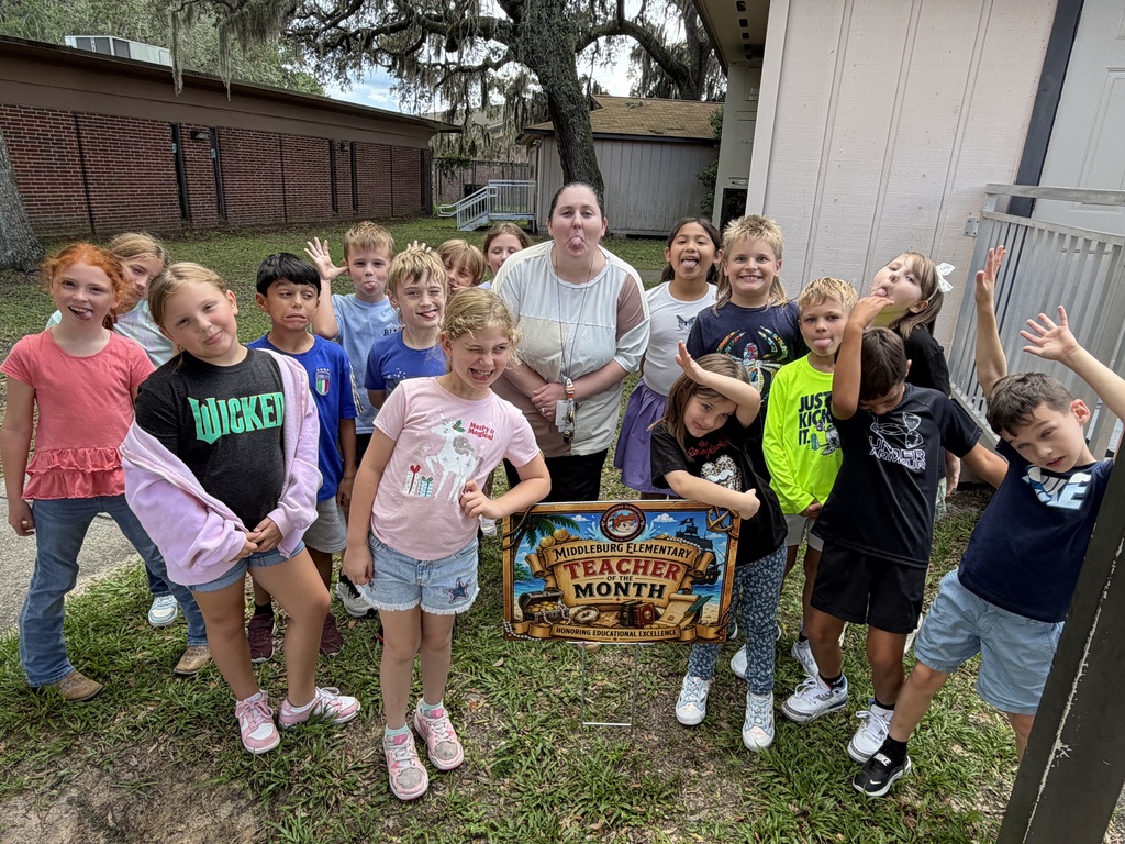 A group of children and an adult woman standing in front of a building with a sign.