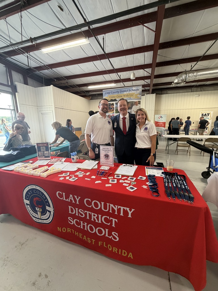 Three people stand behind a table with a red tablecloth, displaying "Clay County District Schools Northeast Florida".