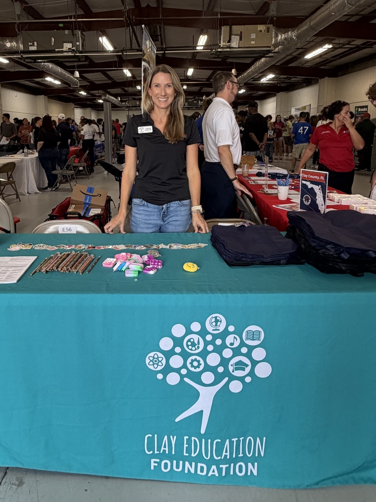 Woman standing at a booth with a teal tablecloth. Logo shows "Clay Education Foundation" with a tree graphic.