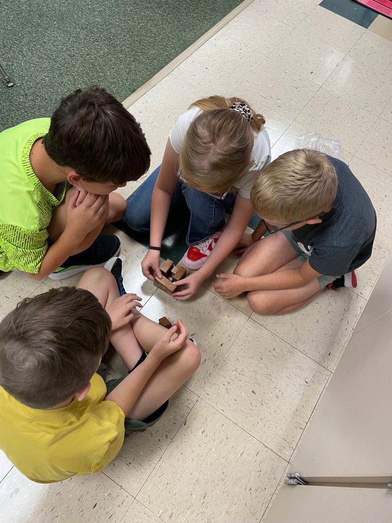 Four kids sit on a tiled floor, engaging in an activity with a small object. One child holds a paper plate.