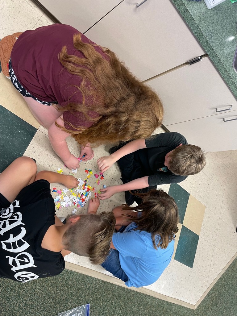 Four individuals, wearing casual attire, are kneeling on the floor, engaging in an activity with colorful puzzle pieces.