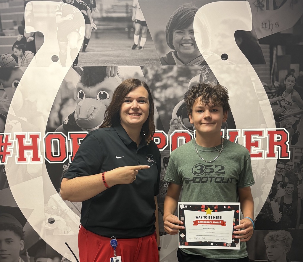 A woman and a boy stand with certificates in front of a horseshoe backdrop with a sports collage.