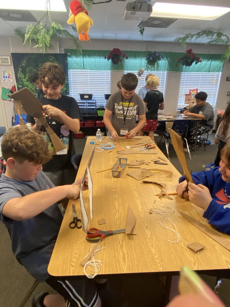 Four boys work on a project together at a long table in a classroom.
