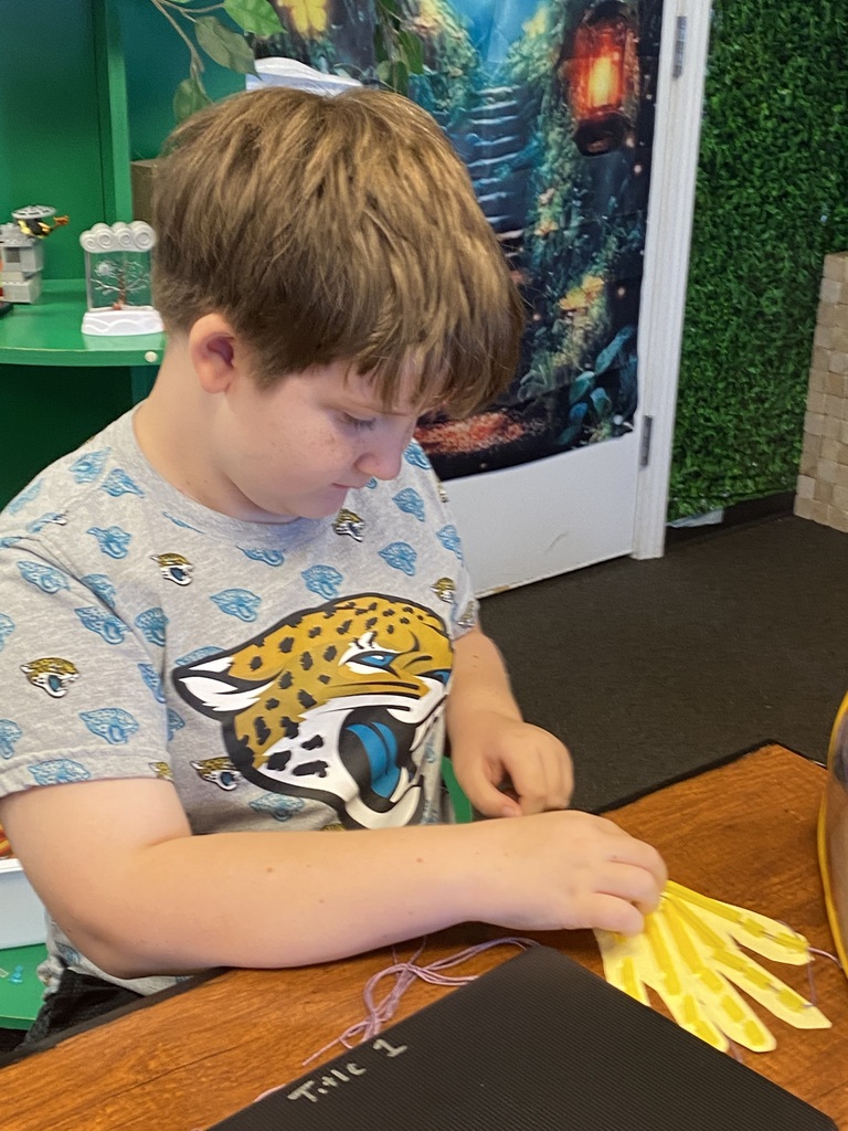 A young boy is sitting at a table, wearing a t-shirt with a cheetah design. He is working on a craft.