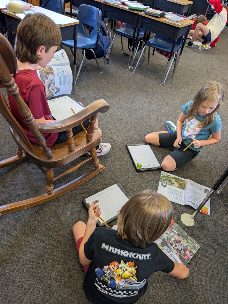 Four children in a classroom setting. One child sits in a wooden chair and the others are on the floor.