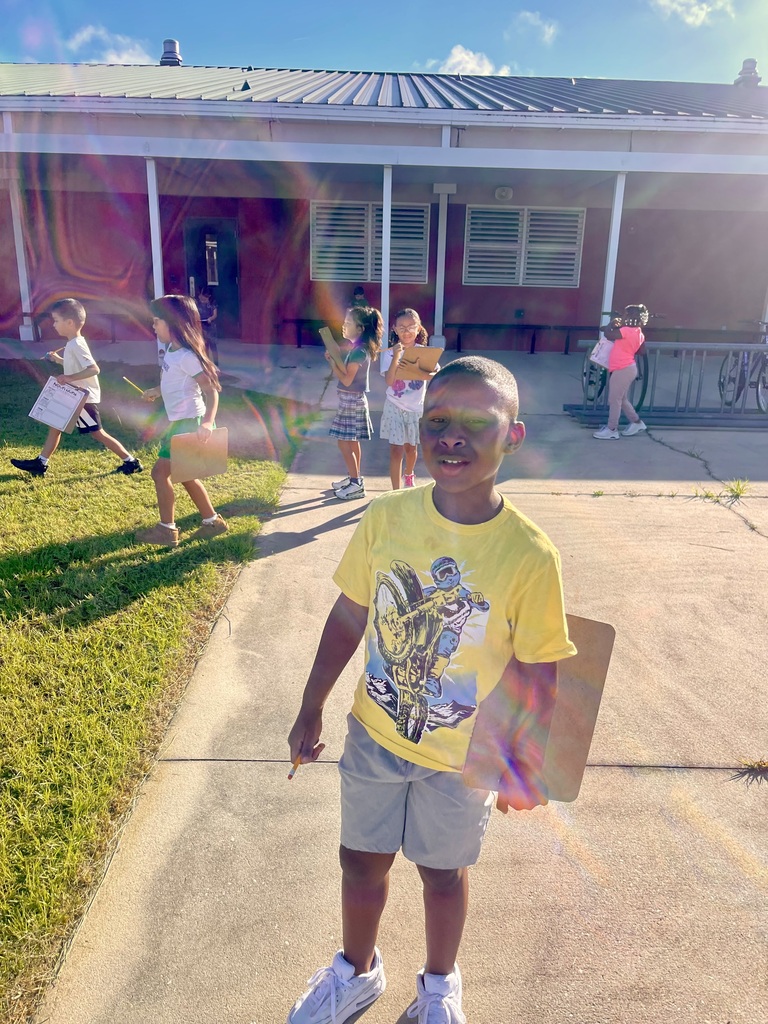 A child in a yellow shirt and shorts holds a board in a driveway. Other children play in the background.