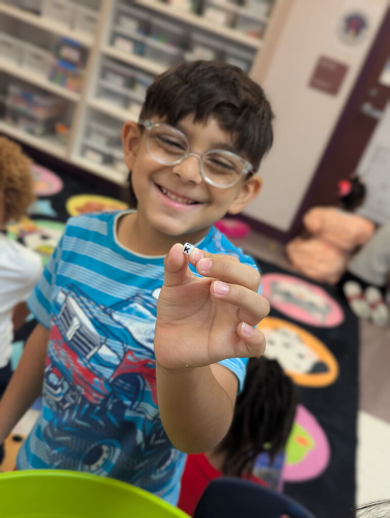 A child shows a small object with the letter K.